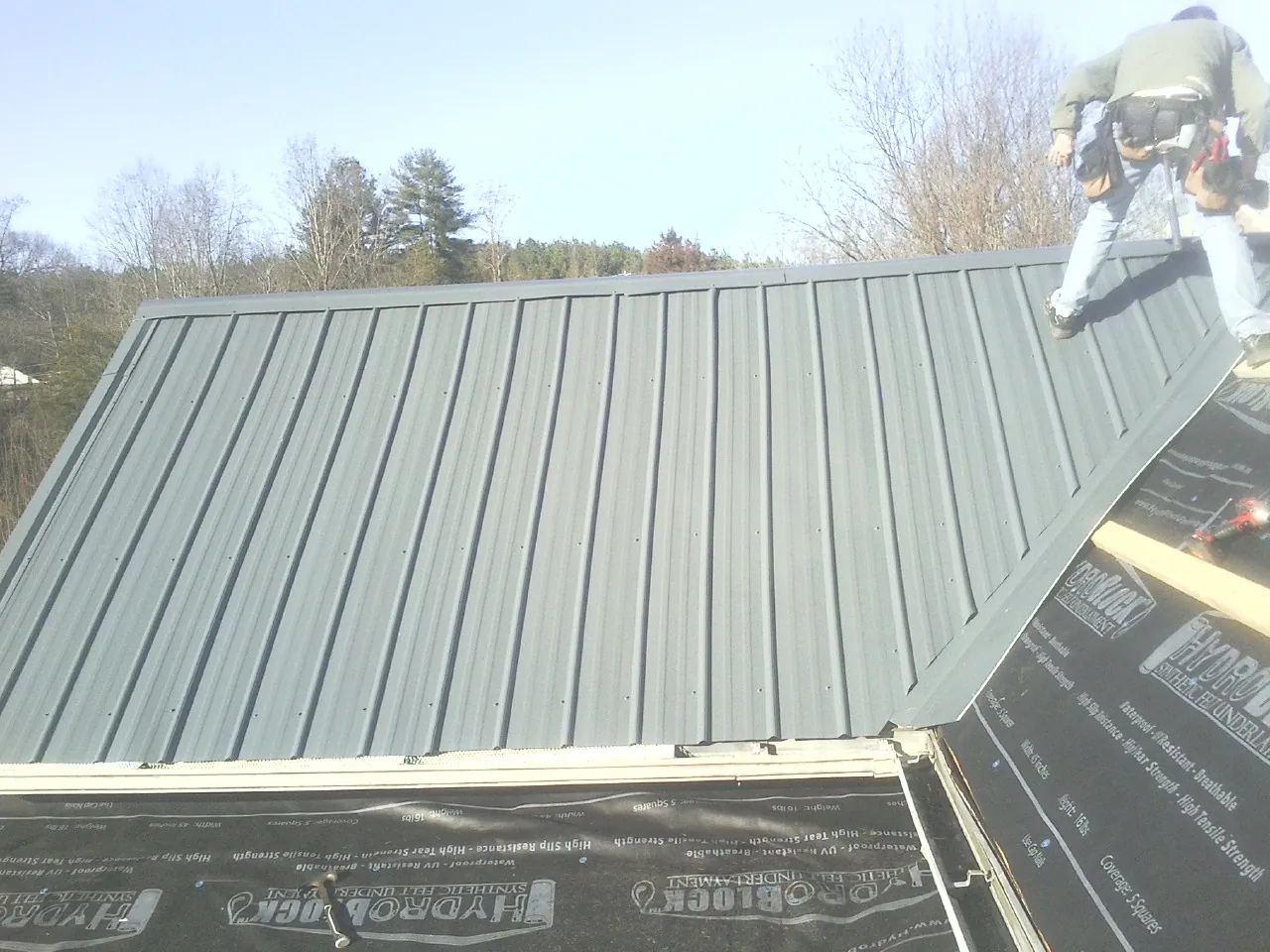 Crew installing dark green standing seam panels over synthetic underlayment in Metamora
