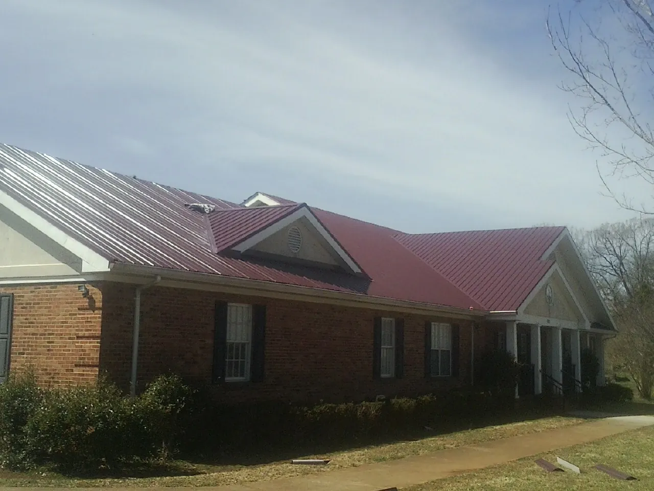 Red metal roof with gabled entries on a long brick building, from a Hail Damage Roof Repair job in Metamora