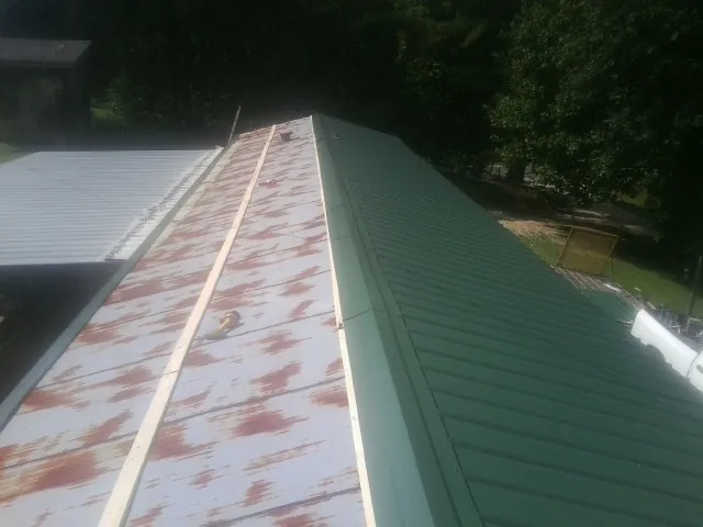 Old rusted panels beside newly installed green metal roofing — Wind Damage Roof Repair by Roofing Brothers in Metamora