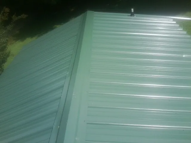 New green metal panels meeting at the ridge of a roof — Flat Roof Repair work by our crew in Metamora